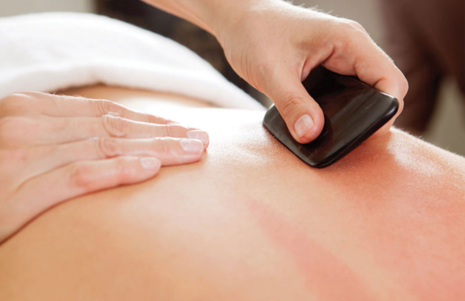A person receiving Gua Sha treatment on their upper back with a practitioner’s hand gently pressing down
